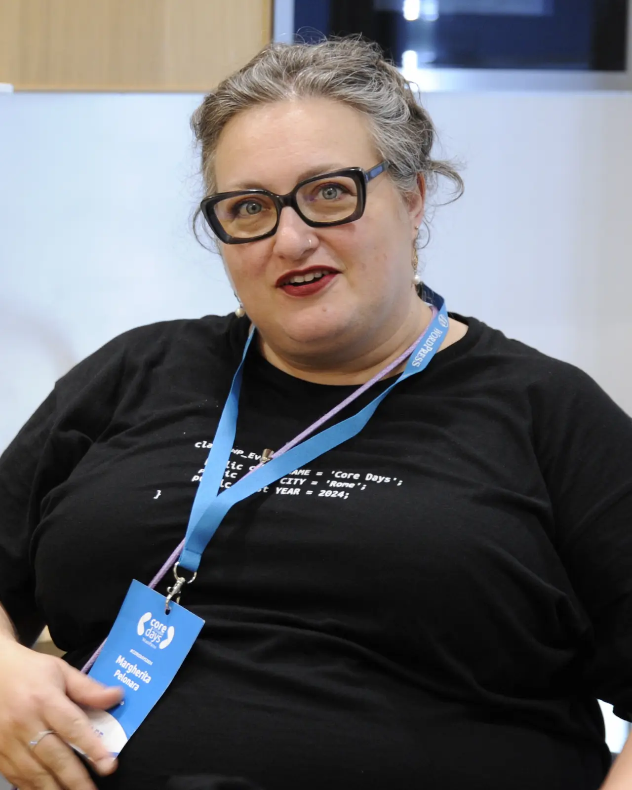 Margherita Pelonara sorride davanti alla fotocamera durante un evento WordPress. Indossa una maglietta nera con codice e un badge con scritto ‘Core Days’.