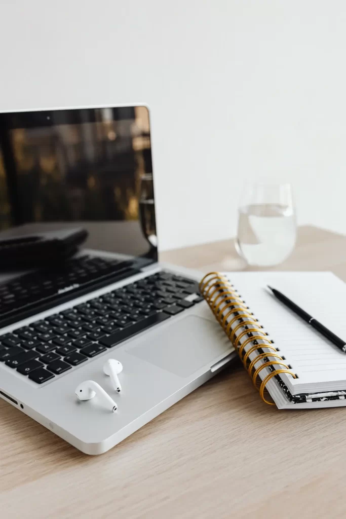 Una scrivania essenziale con laptop, taccuino e penna: uno spazio di lavoro silenzioso dove le idee prendono forma.